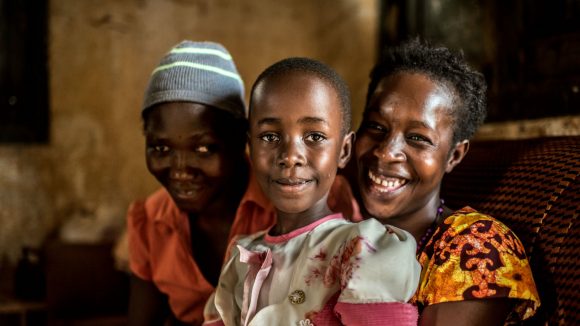 A woman, smiling, hugs her daughter and best friend.