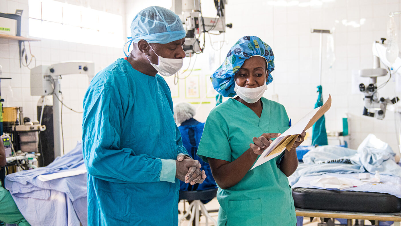 Dr Msukwa discusses paperwork with an eye health nurse while wearing surgical scrubs.