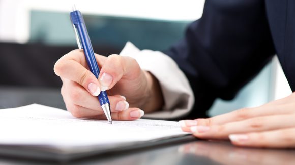 A close-up of a woman's hand holding a pen as she signs a document.