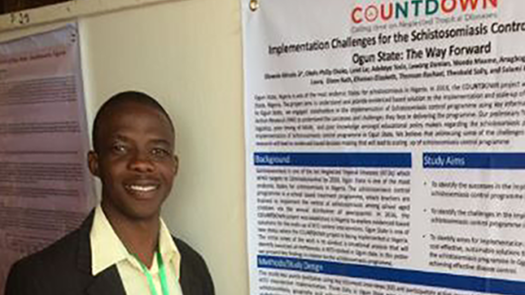 Dr Akinola Stephen standing next to a poster about Countdown's work on NTDs.