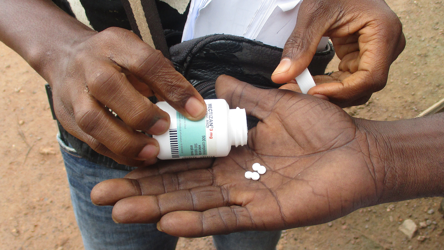 A volunteer places medication in a man's outstretched hand.