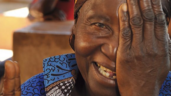 From the cover of Sightsavers annual report 2011: a woman smiling as she covers one of her eyes.