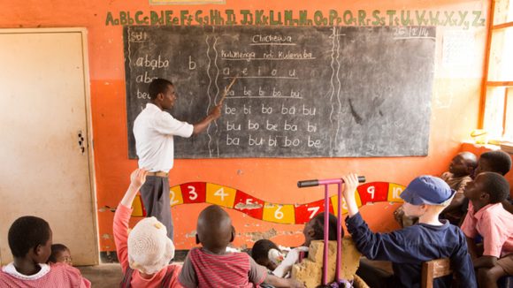 A teacher writing on a blackboard in front of a group of children.