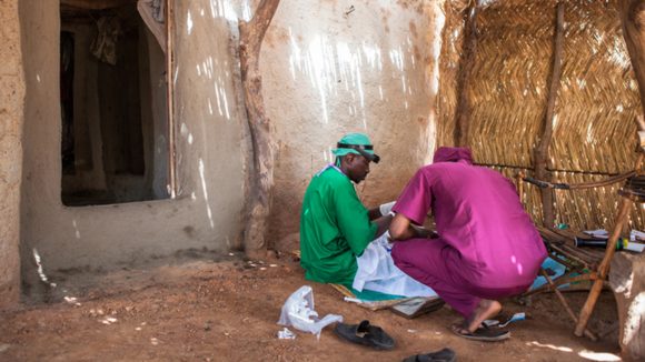 Boubacar Fomba carrying out trachoma surgery on the floor in someone's home.