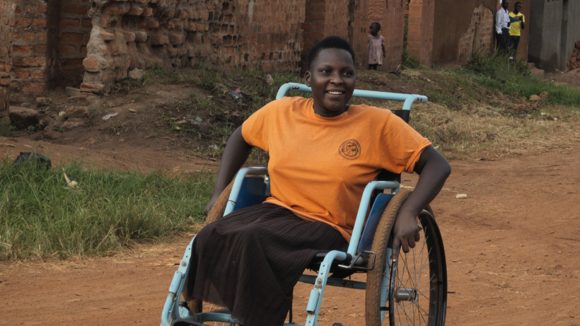 A young woman sitting in her wheelchair on a dirt road.