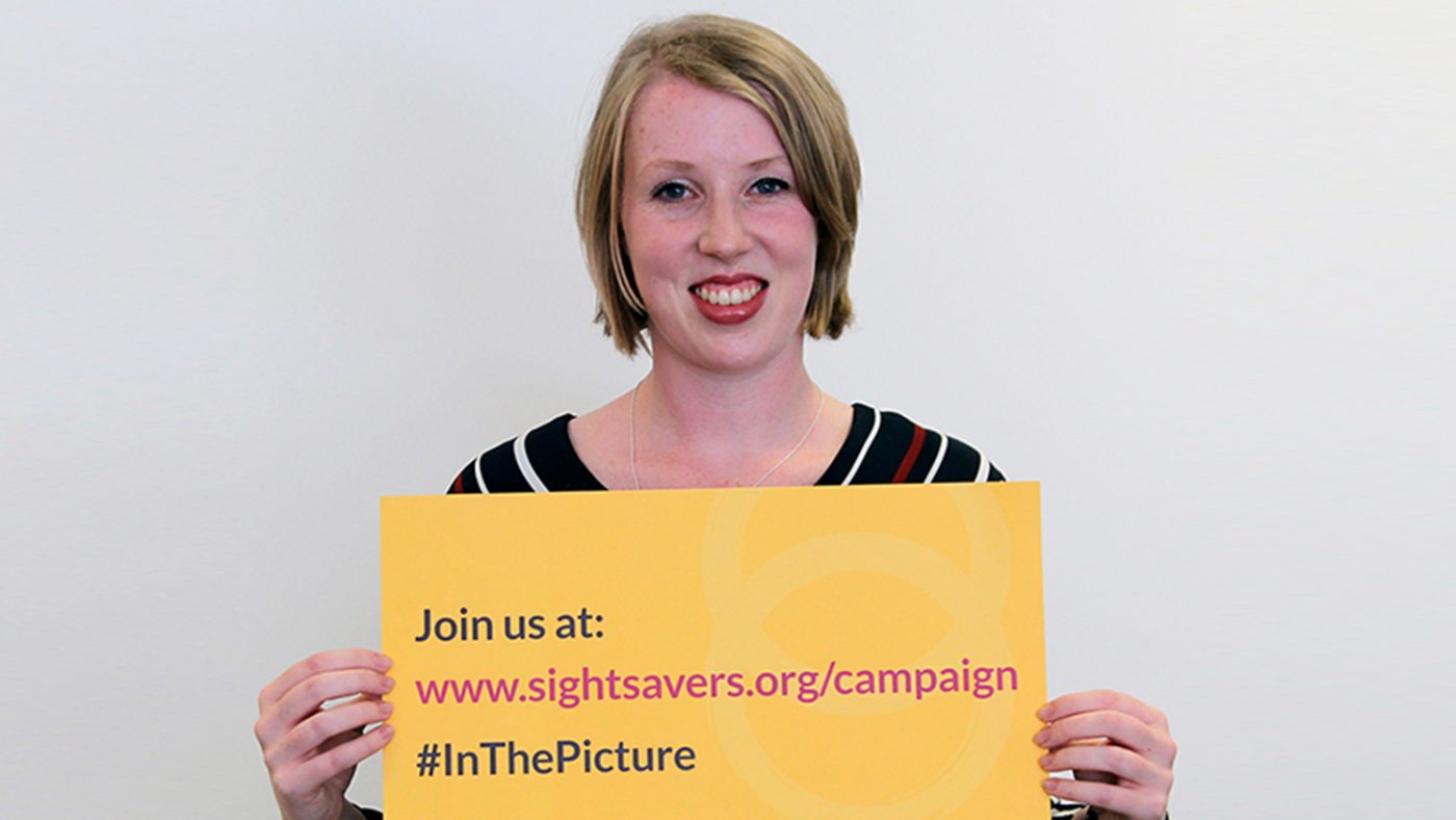 Paralympian Georgie Bullen holds a yellow sign containing the words: 'Join us at en.sightsavers.co/campaign, #inthepicture'.