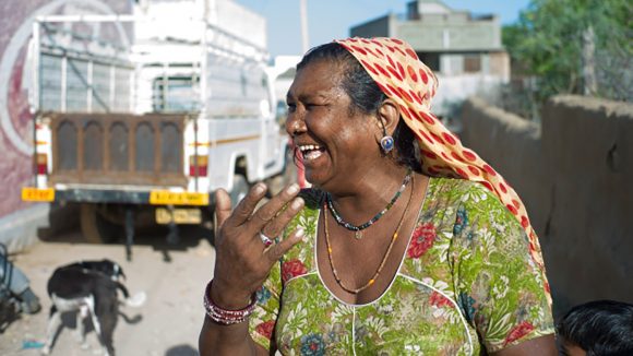 A woman in New Delhi, India, laughs as she stands on the street in front of a truck.