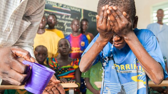 A schoolboy splashes water on his face to learn about facewashing, as part of a SAFE initiative in Senegal.