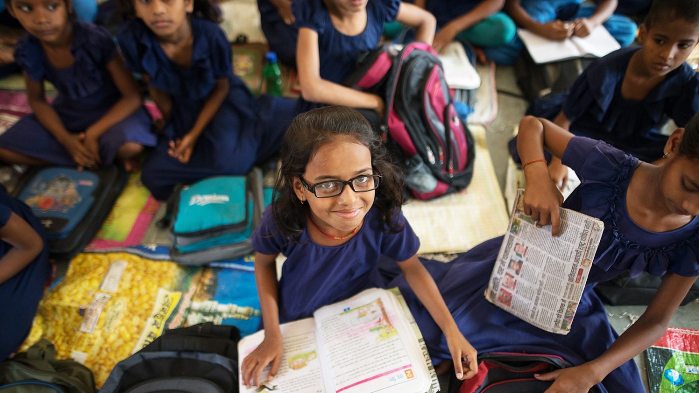A girl with glasses smiles with a book on her lap.