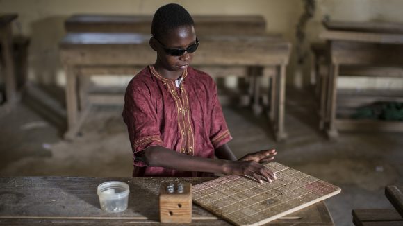 Mohamed sits in the classroom reading braille.