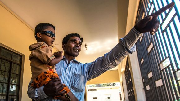 Four-year-old Arman smiles in his new dark glasses, as he's held by his father after his cataract surgery in Bangladesh.
