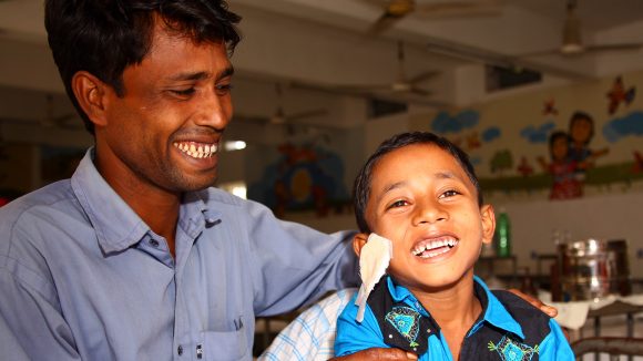 A boy smiles and is embraced by his father after having his dressings removed following eye surgery in Bangladesh.
