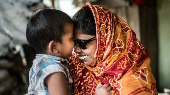 A smiling mother with a visual impairment hugs her young son.