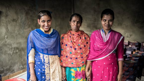 Three smiling women take a break from their packaging business.