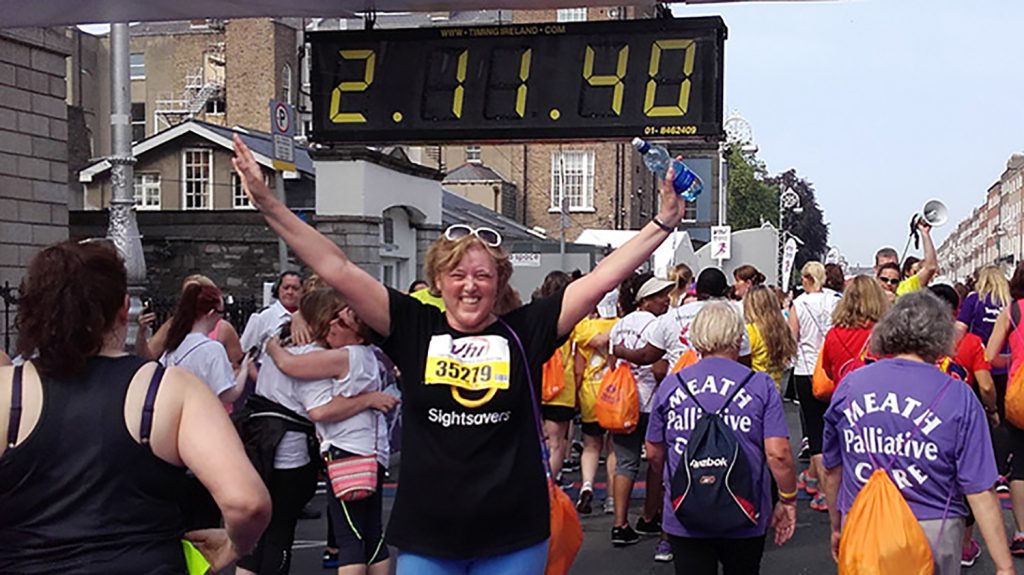 Jackie Carroll raises her arms at the finish line of the VHI Mini Marathon, standing underneath the clock reading 2:11:40.