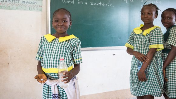A schoolgirl holds a tablet in her hand and smiles.