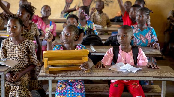 A girl raises her hand in class to answer a question.