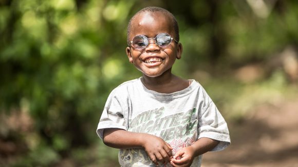 Criscent proudly wearing his new glasses, as he stands in some woods on the way to his village in Uganda.