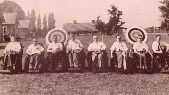 The archery competitors from the Stoke Mandeville Games line up on the field in front of their archery targets.