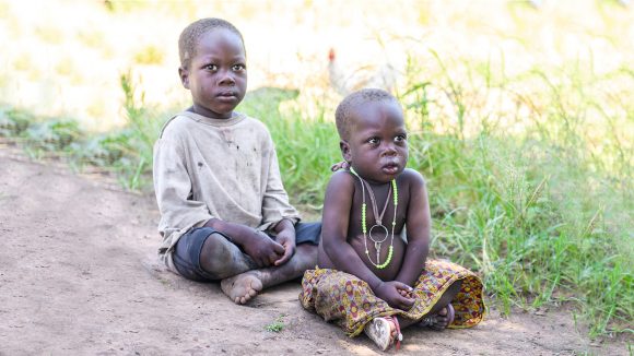 Young Adoc and Obali sit on the floor in their village.