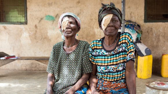 Sisters Barikisu and Ayishetu sit outside their home with bandages covering their eyes, following their trachoma operation.