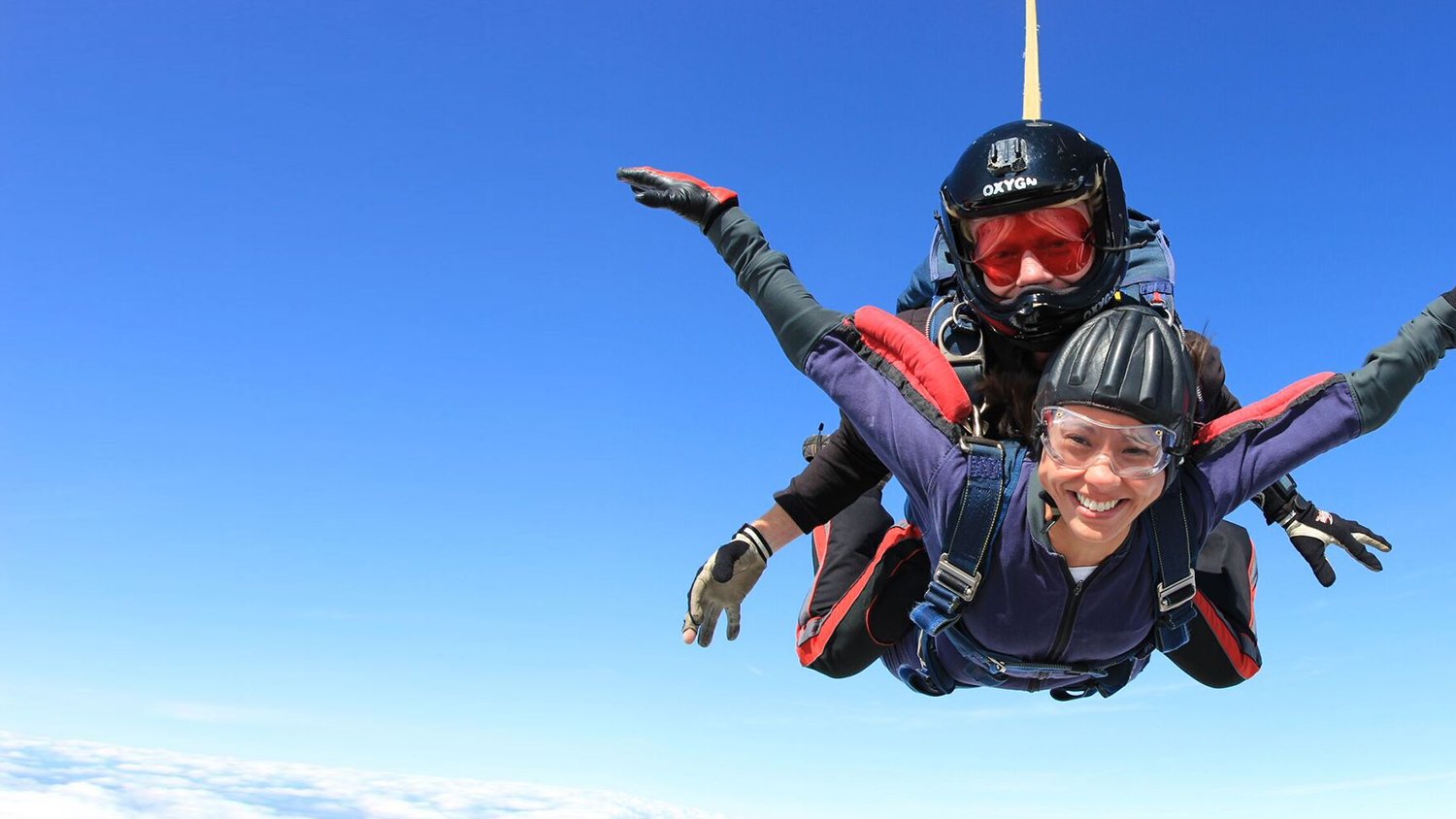 A woman grins during her skydive as she freefalls while attached to her instructor.