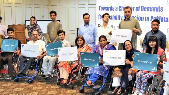 A group of representatives from disabled people's organisations hold up signs saying 'Make it count'.