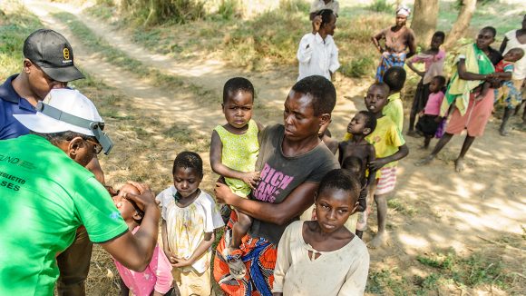 A man examining a child's eyes. with a que behind.