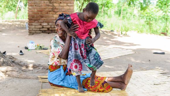 A grandmother is helping her young granddaughter stand.