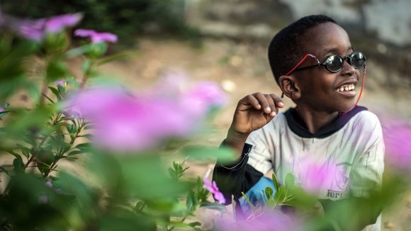 Fahad smiles while wearing sunglasses as he sits beside a colourful bush.
