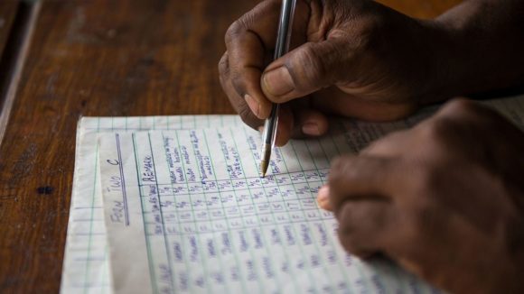 A close-up of a researcher's hands as they write data onto a sheet of paper.