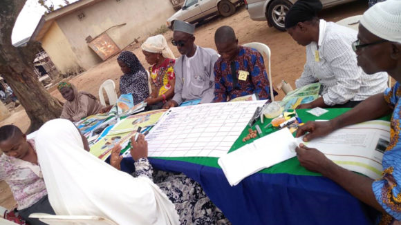 A group of volunteers sit around a table in a village in Nigeria.