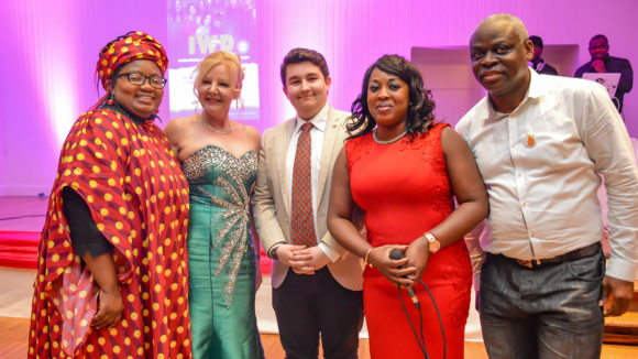 A group of guests in colourful formal clothes smile at the camera.