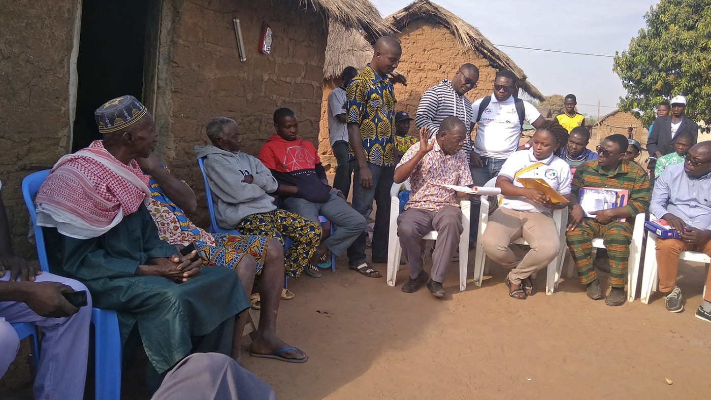 A group of people sit outside a hit in a village in Cote d'Ivoire.