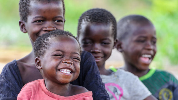 Two-year-old Nalukena smiles broadly with a group of other children.