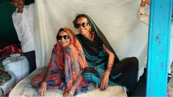 two ladies sitting and smiling wearing sunglasses.
