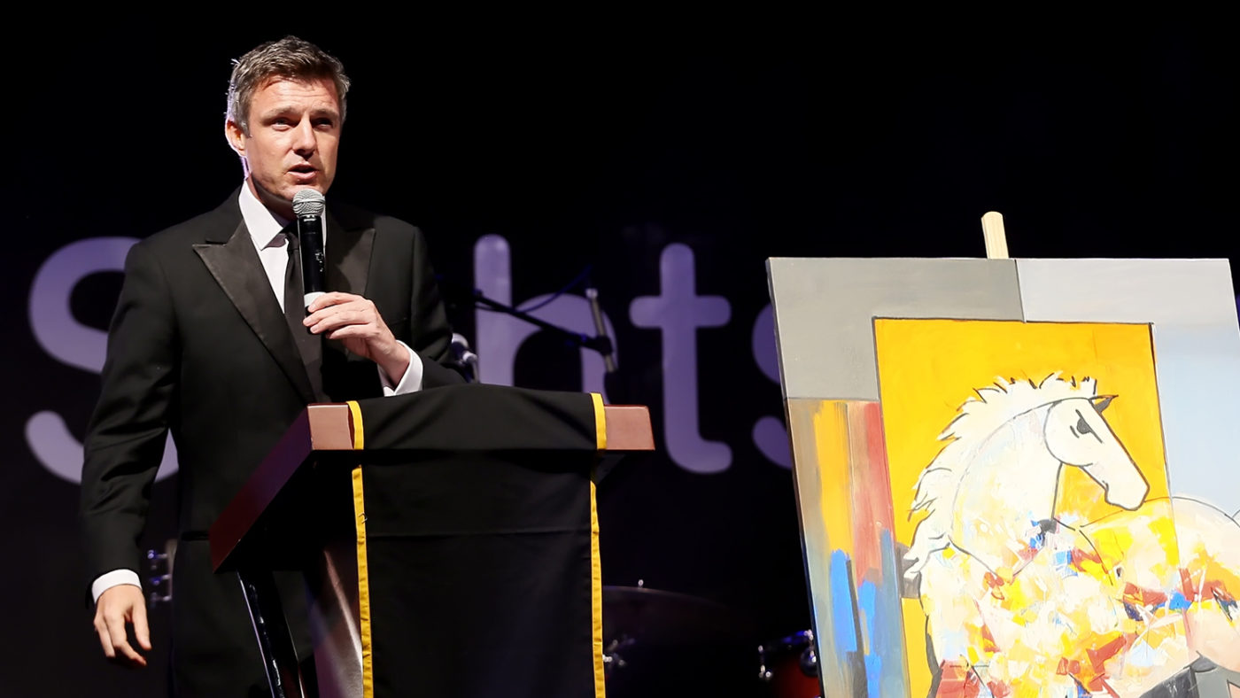 Tom Urquhart on stage, holding a microphone.