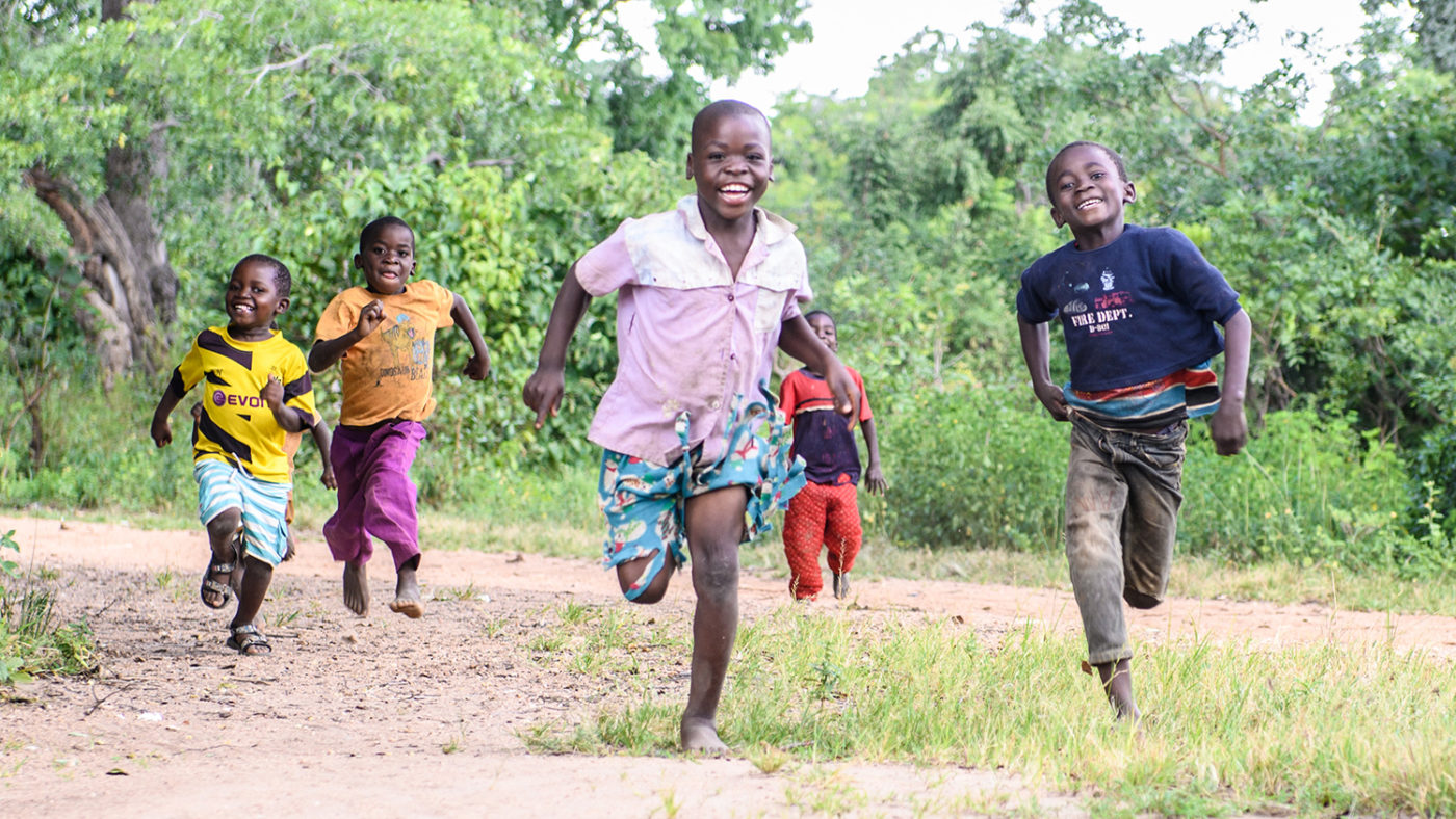 A group of children smile and run through their village.