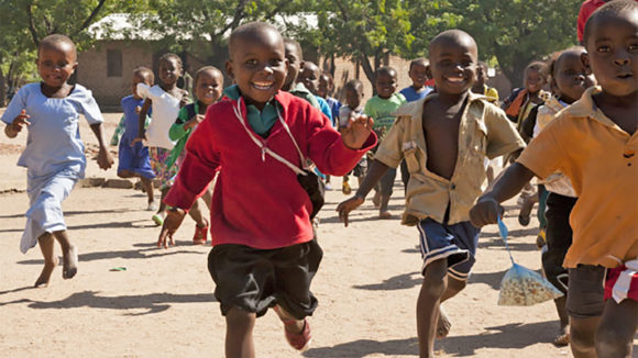 Young school pupils run in the playground, while smiling happily.