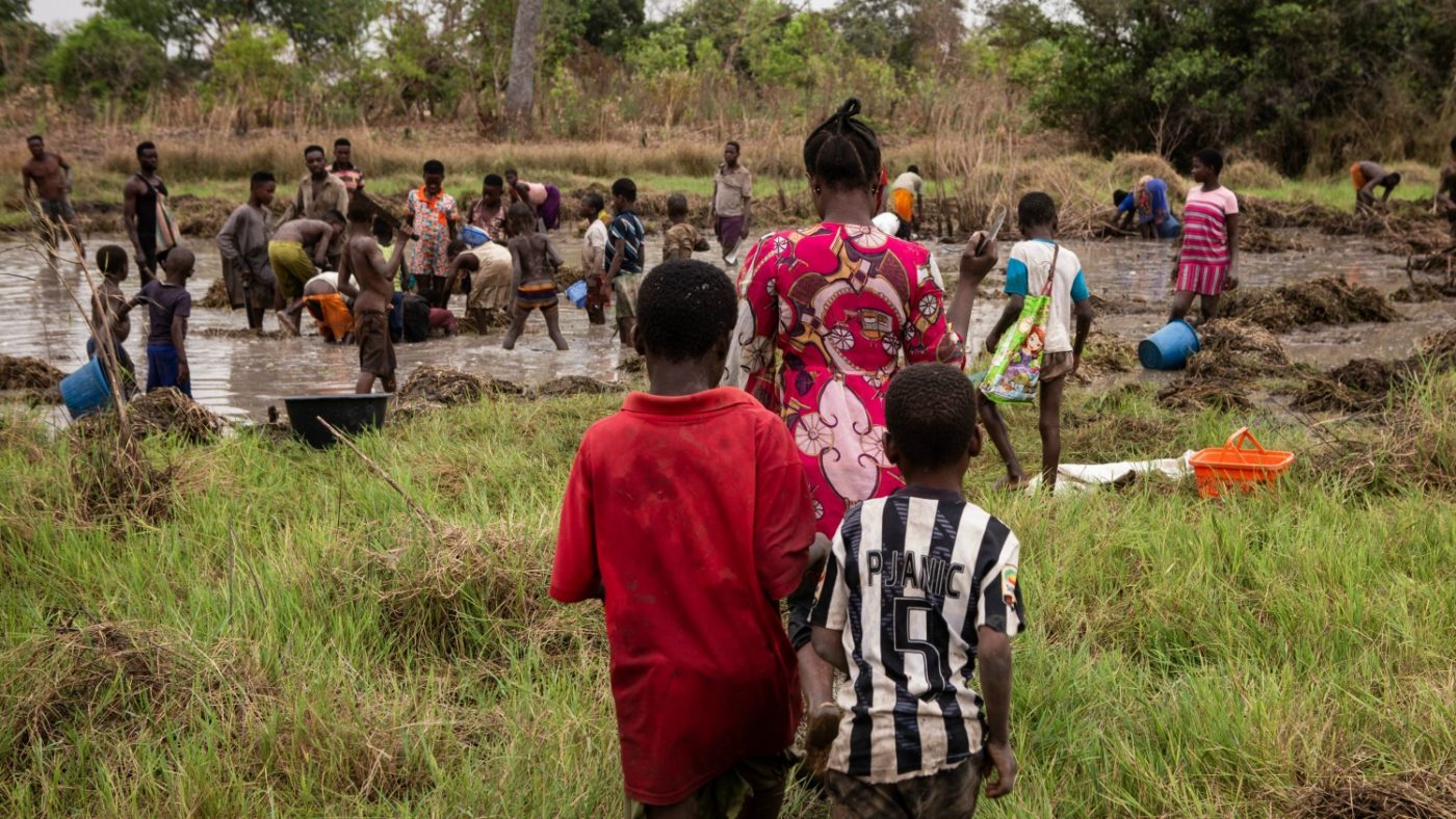 A family walks to the river which is full of people bathing.
