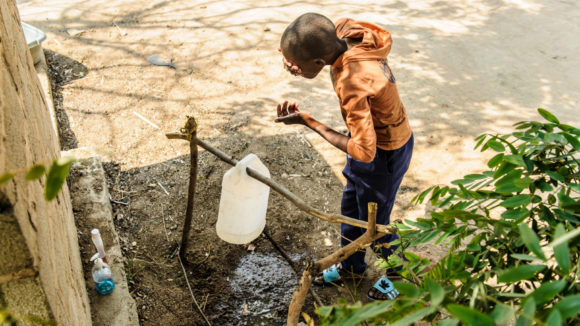 A boy washes his face using a tippy tap, a hygienic handwashing device in areas where clean water is scarce.