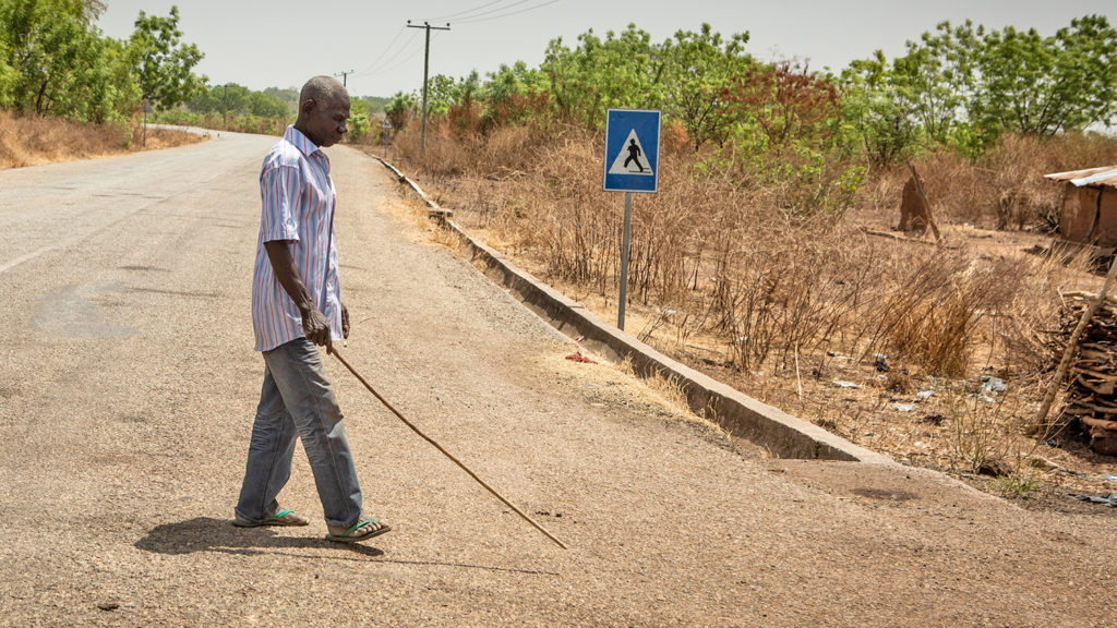 Akwasi walks with a stick near his home in Asubende.