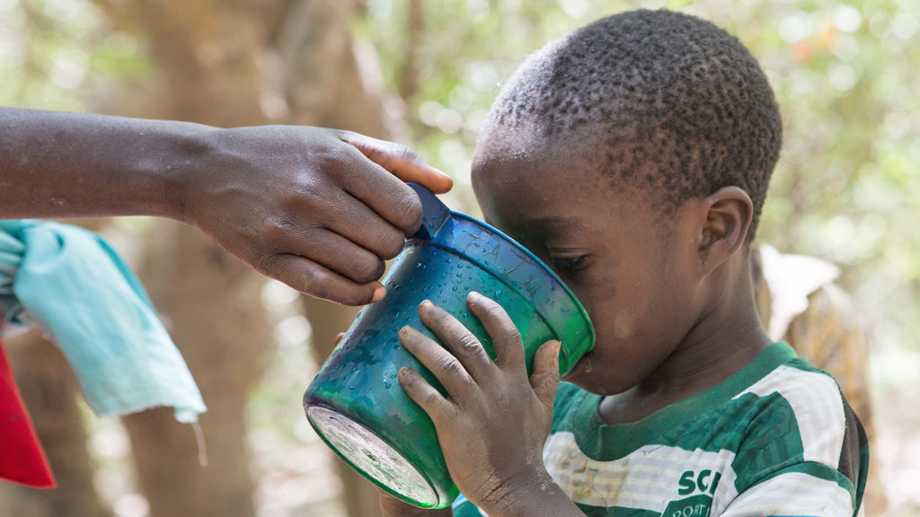 A child drinks water from a cup during a drug administration session in Nigeria.