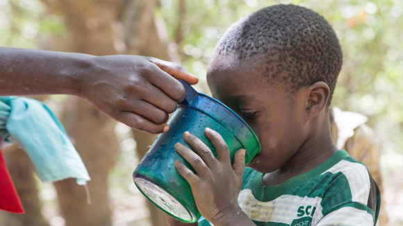 A child drinks water from a cup during a drug administration session in Nigeria.