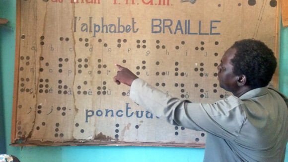 A teacher in Mali points to a sign showing the braille alphabet.