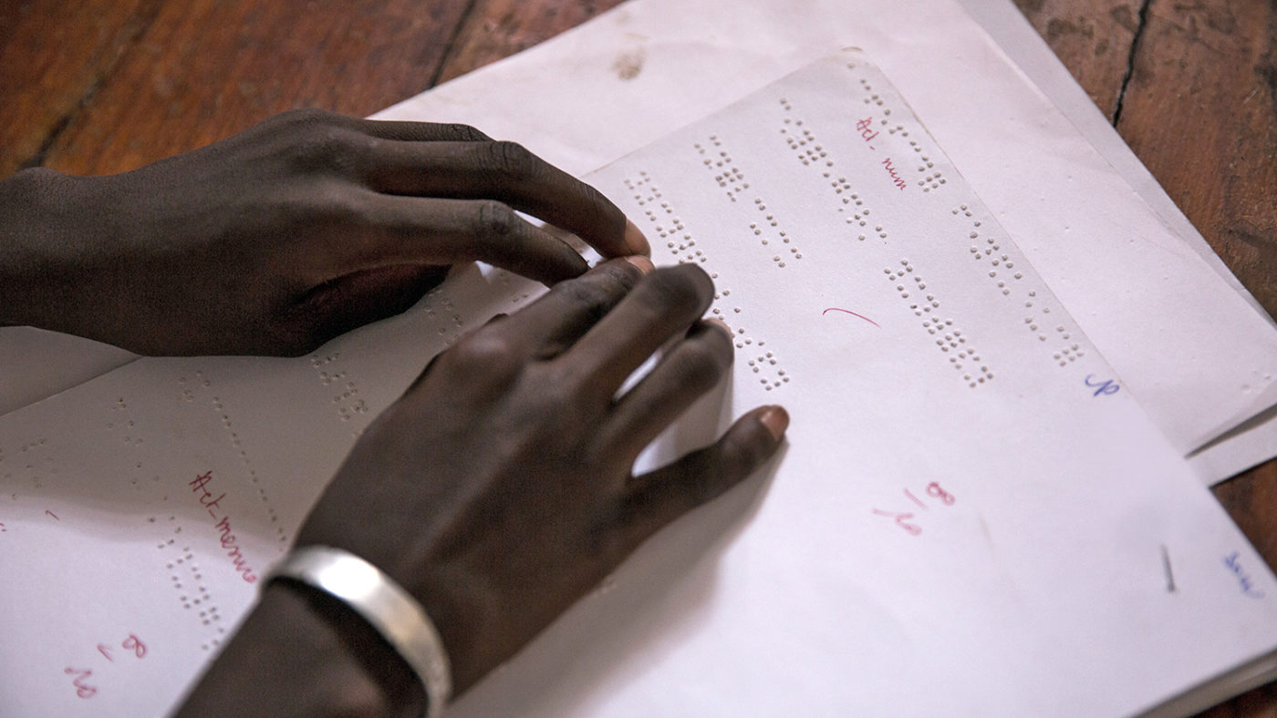 A girl from Senegal reads braille in the classroom.