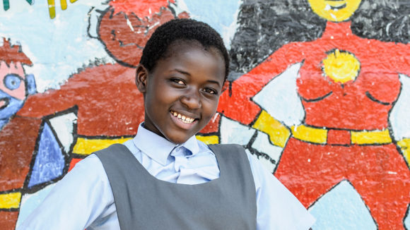 A school student in Zambia stands in front of a mural depicting superhero characters from Sightsavers' Super School of 5 programme.