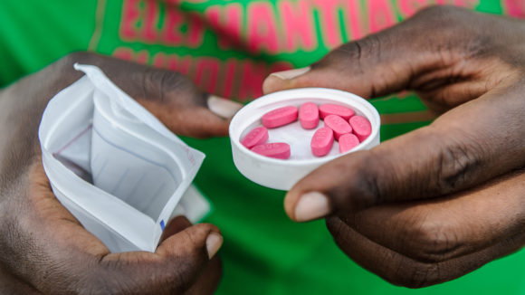An eye health worker holding some pink tablets.