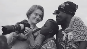 Kate Holt holding her camera and showing the screen to two smiling African children.