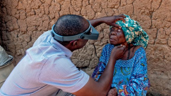 Trachoma surgeon checks the eyes of a patient for signs of trachoma outside her home in Benin.